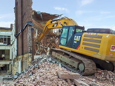 Yellow YORK1 excavator on a pile of building debris, completing a building demolition