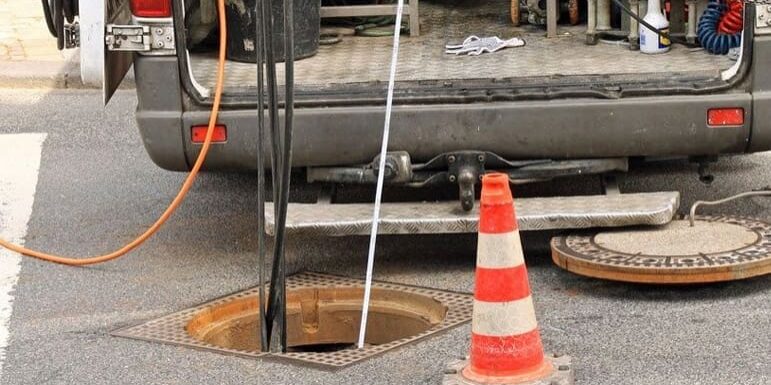 Back of an open work van parked at a sewer grate, wiring in sewer for inspection