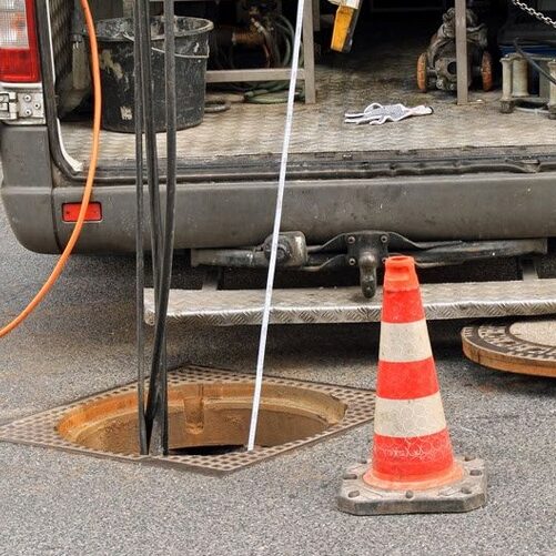 Back of an open work van parked at a sewer grate, wiring in sewer for inspection